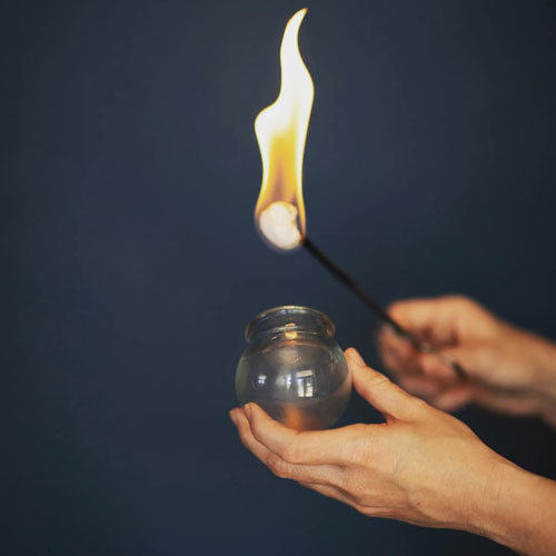 Hands hold a glass gar and a fire source for cupping.