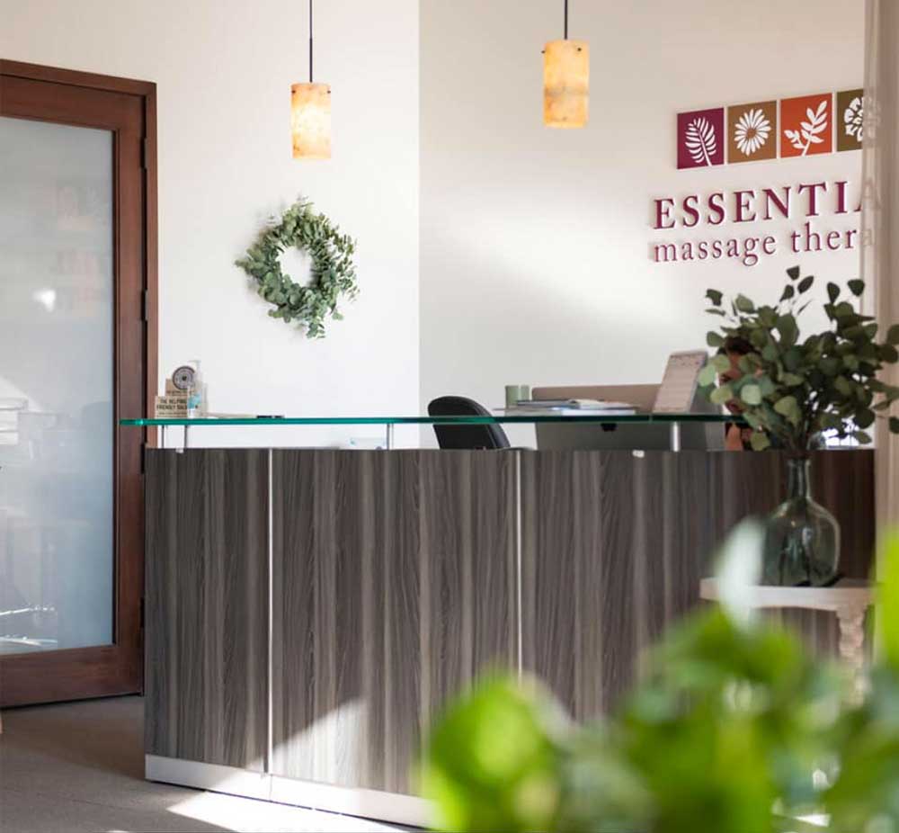 A photo of the main desk at Essential Massage Therapy in Ferndale, Michigan. The logo is behind the desk and plants, a wreath are visible.